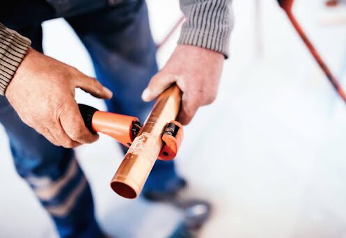 A plumber cutting a copper pipe with a pipe cutter.