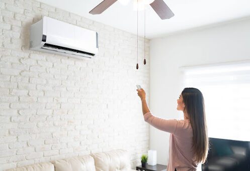 A woman using a remote to control an indoor ductless AC unit on a wall in a home.
