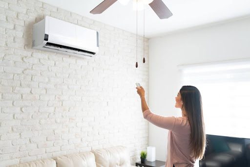 A woman using a remote to control an indoor ductless AC unit on a wall in a home.