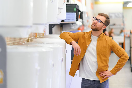 Man resting his elbow on a water heater as he contemplates which model to buy